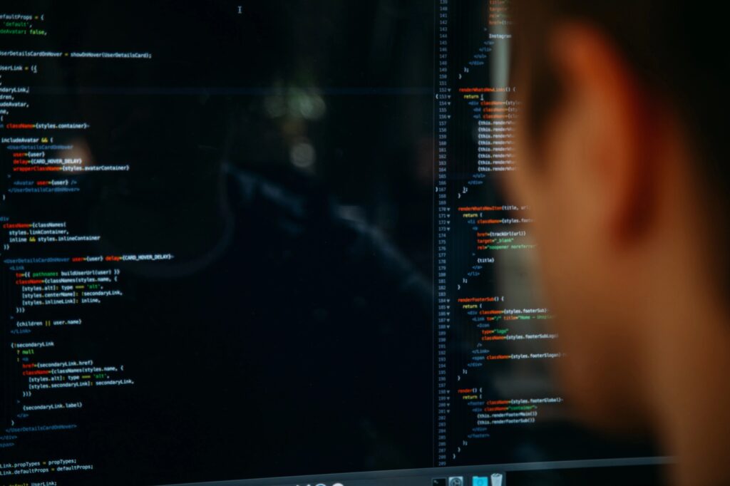 The blurred side of a man's head as he looks at a split screen of coding.