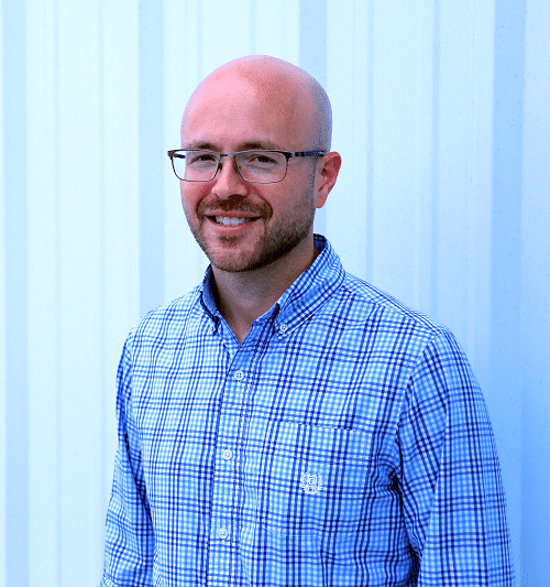 A headshot of Kris Adams: A middle-aged bald man wearing a blue plaid shirt.