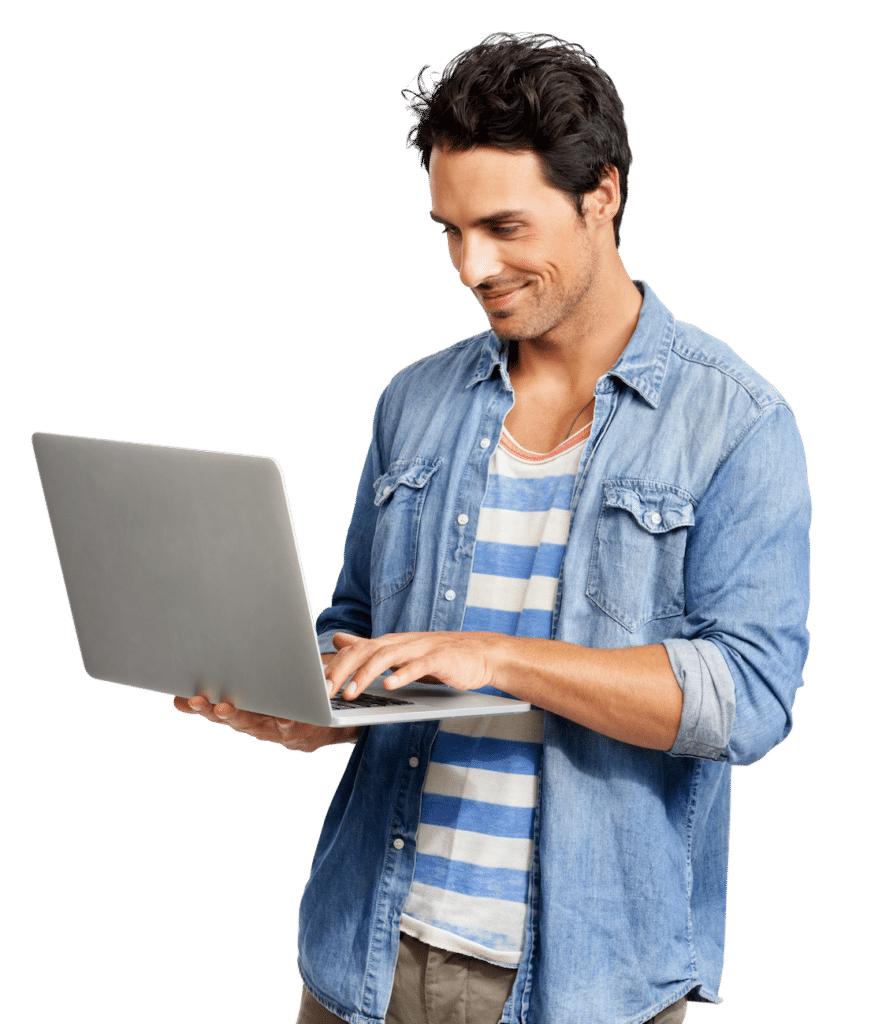 A man wearing a blue and white striped T-shirt underneath a chambray shirt, stands and holds a silver laptop.