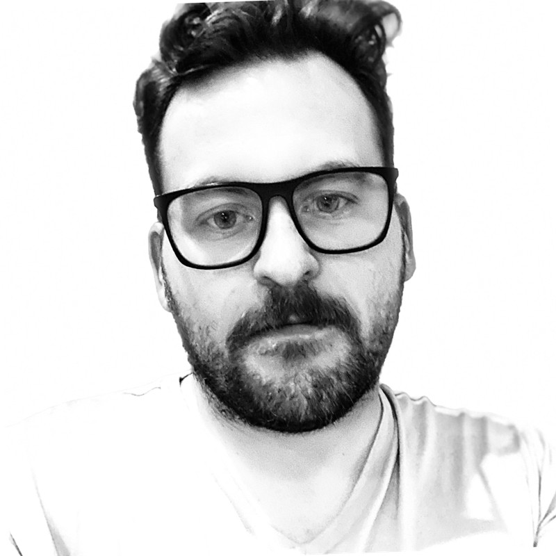 A black and white headshot of Casey Kinsey, awhite man wearing glasses with dark hair.