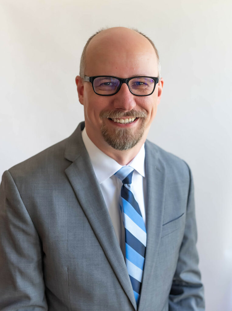 A headshot of Eric Wall, a bald man in a gray suit.
