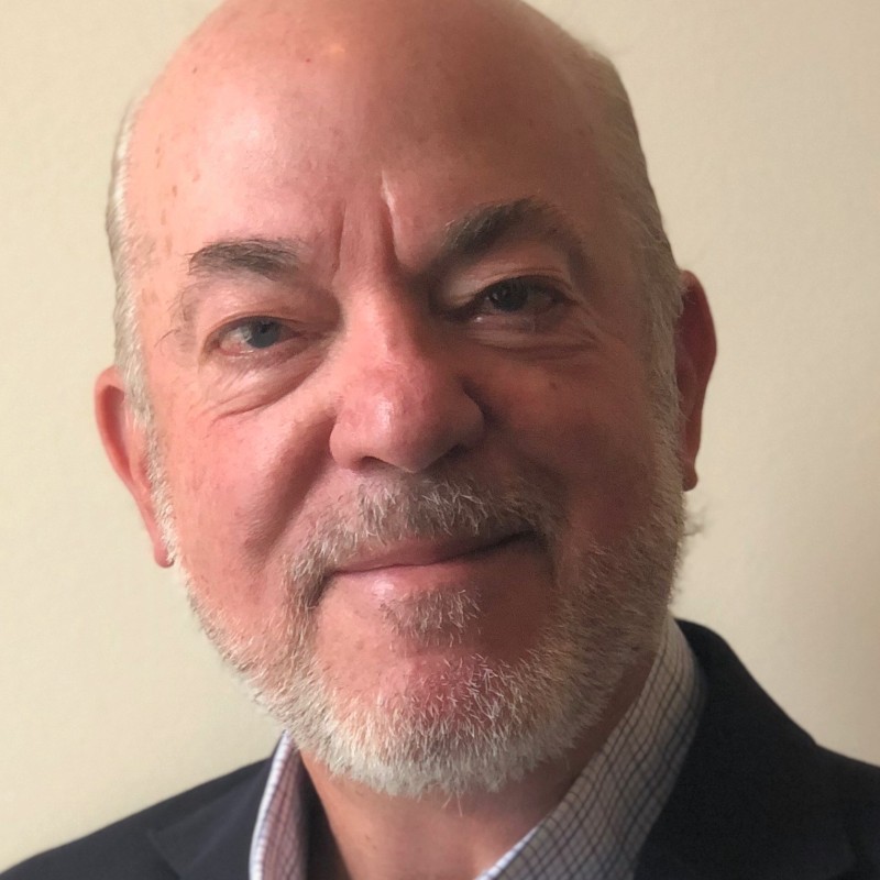 A headshot of an older bald man with a white beard.