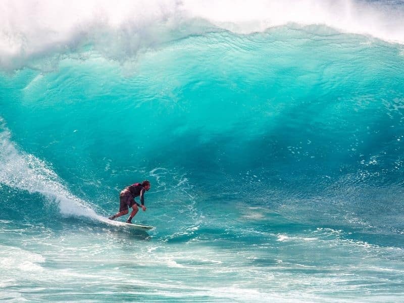 A surfer beginning to surf through the tunnel of a light blue wave beginning to crash down.