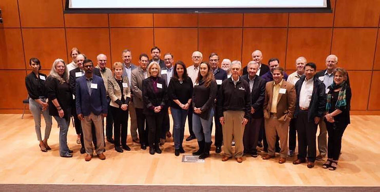 A group of middle aged people dressed in business casual and wearing name tags standing on a stage.