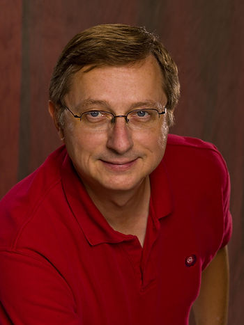 A headshot of a man in his 50s or 60s wearing glasses and a red polo.