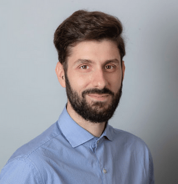 A headshot of a white man with brown hair and a beard wearing a blue button-up.