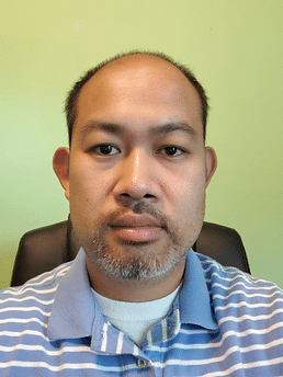A headshot of an Asian, balding man wearing a blue and white striped shirt sitting in an office chair.