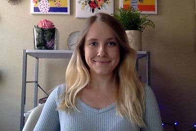 A headshot of a blonde woman sitting in an office chair wearing a blue shirt.