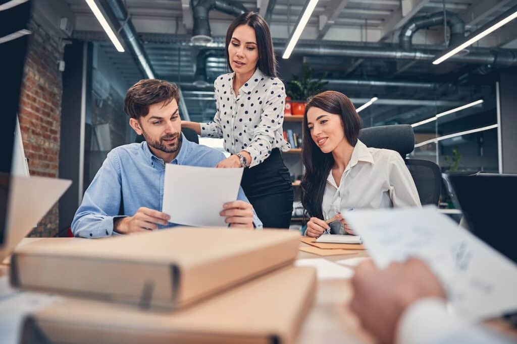 Young smiling employees working in a modern office at table with documents. Three employees and dressed in business casual and are examining one doument of job search tips.